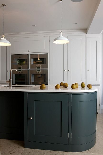a chic modern kitchen with white shaker style cabinets, a dark green curved kitchen island, pendant lamps