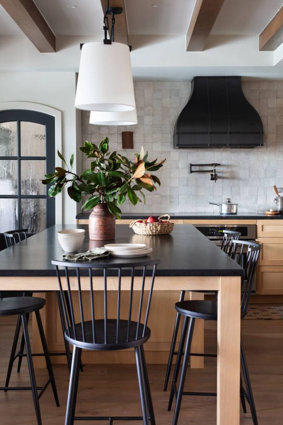a chic vintage-inspired kitchen with stained shaker cabinets and a large table kitchen island, black statement countertops, a black hood and black chairs