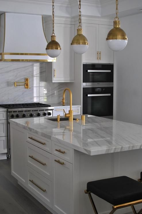 a chic white kitchen with shaker cabinets and a kitchen island, a white quartz backsplash and countertops plus touches of gold