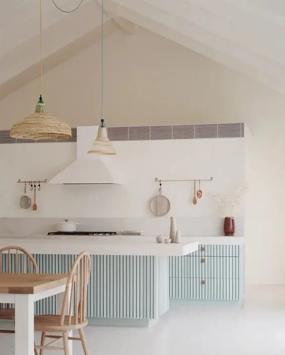 a coastal kitchen with pale blue ridged cabinets and a kitchen island, woven pendant lamps and a white hood that matches the backsplash