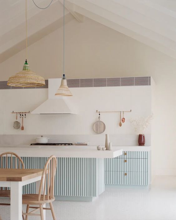 a coastal kitchen with pale blue ridged cabinets and a kitchen island, woven pendant lamps and a white hood that matches the backsplash