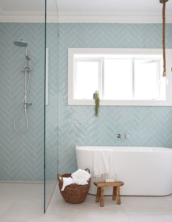 a contemporary bathroom with dusty blue herringbone tiles, an oval tub, a shower, a basket and a stool is welcoming