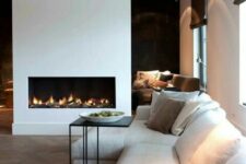 a contemporary living room with a neutral sofa, a black side table, a minimalist white fireplace and some lights