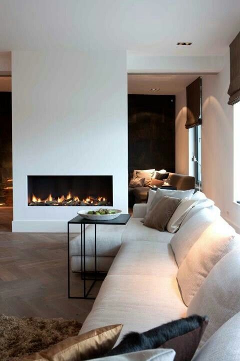 a contemporary living room with a neutral sofa, a black side table, a minimalist white fireplace and some lights