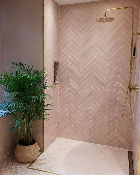 a contemporary pink bathroom clad with pink tiles in a herringbone pattern, gold fixtures and frames for a glam look