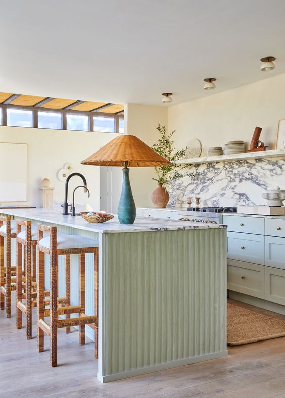 a cozy and welcoming mint green kitchen with shaker style cabinets, an open shelf instead of upper ones, a white marble backsplash, a fluted kitchen island