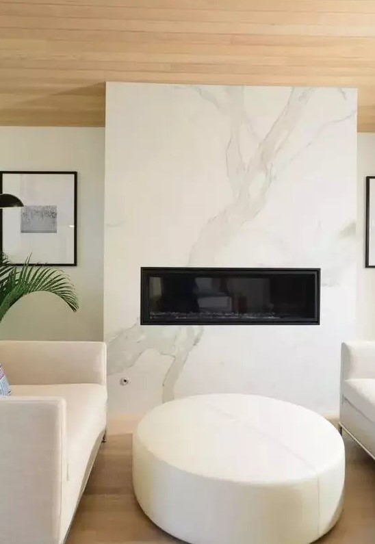 a cozy minimalist space with a white marble fireplace, neutral furniture and a wooden ceiling is very chic