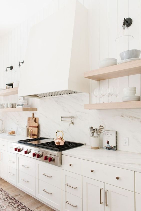 a creamy and airy kitchen with shaker cabinets, a white quartz backsplash and countertops, wooden shelves and a large hood