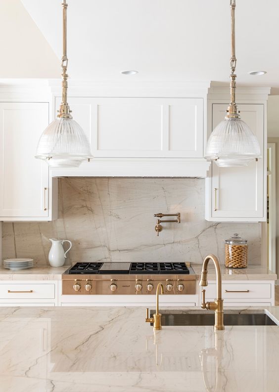 a creamy kitchen with shaker cabinets, a neutral quartz backsplash and countertops, vintage glass pendant lamps