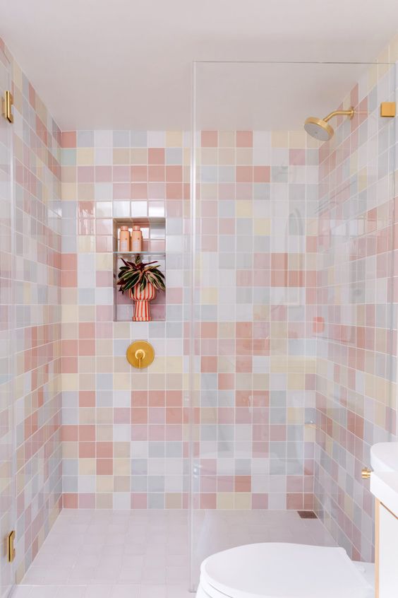 a creative bathroom with mismatching pastel tiles in the shower, white appliances and a gold shower head