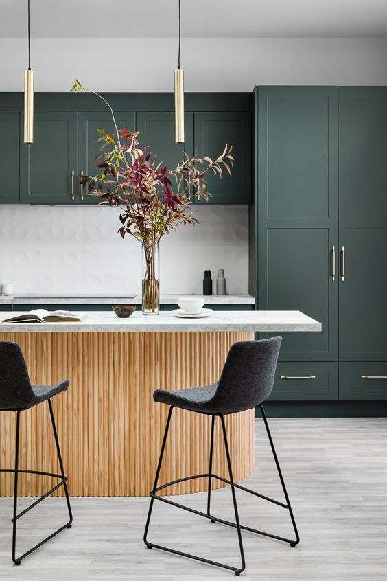 a dark green kitchen with gold fixtures, a fluted kitchen island with white stone countertops, black stools