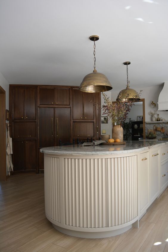 a dark-stained kitchen with a light-colored fluted curved kitchen island that contrasts the cabinetry and stainds out in its backdrop