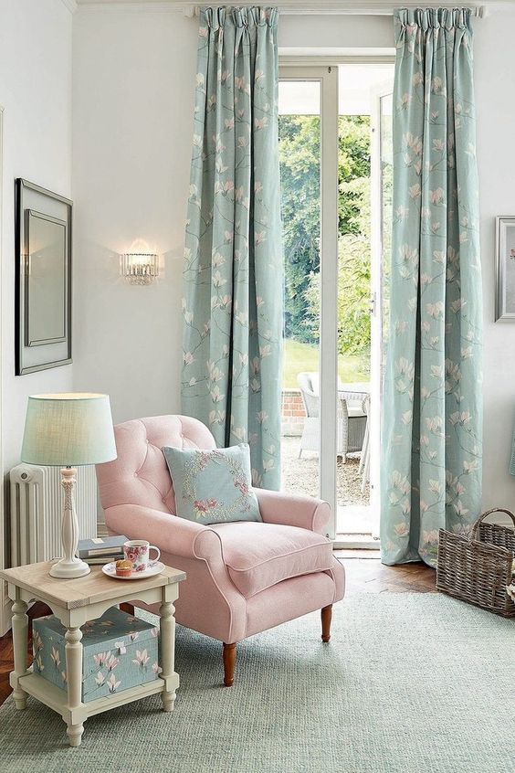 a delicate Provence living room with neutral walls, a pink chair with a blue pillow, blue floral curtains and a box, a mint green rug