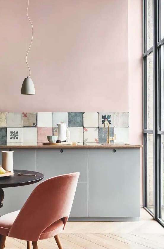 a delicate pastel kitchen with blush walls, grey cabinets, a mismatching tile backsplash and a small eating zone