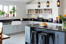 a farmhouse kitchen wiht light grey shaker cabinets, a slate grey kitchen island, black countertops and a white subway tile backsplash
