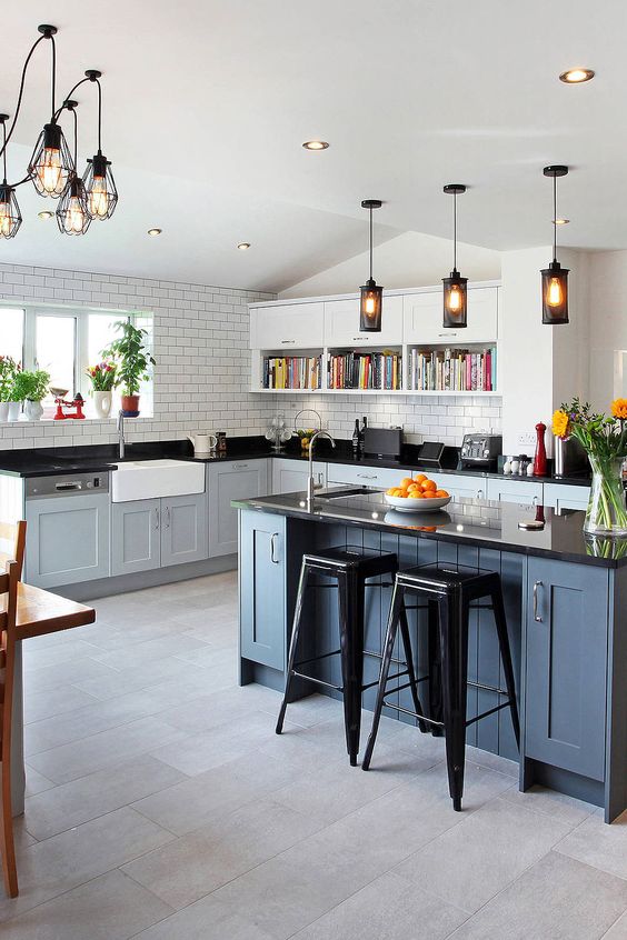 a farmhouse kitchen wiht light grey shaker cabinets, a slate grey kitchen island, black countertops and a white subway tile backsplash