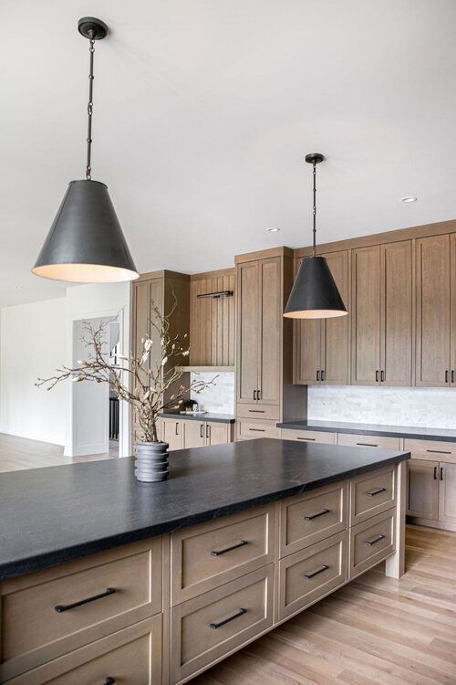 a farmhouse kitchen with stained cabinetry, a white tile backsplash, black countertops and black pendant lamps