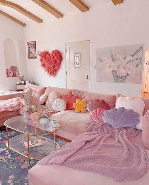a feminine living room with a pink sofa, pastel pillows and blankets, a fluffy pink heart and a tiered glass table