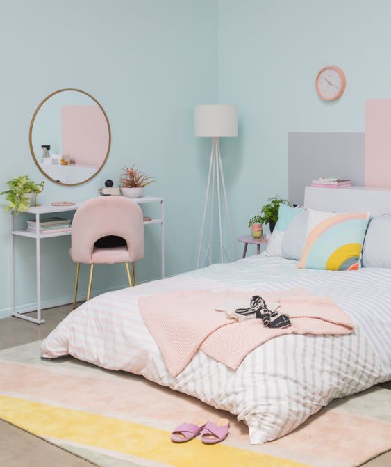 a fun pastel bedroom with blue walls, a low bed with pastel bedding, a console table and a pink chair, a pastel rug
