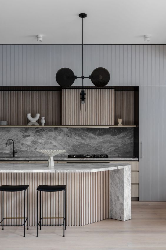 a gorgeous contemporary kitchen with stained and grey slat cabinets, a grey marble backsplash,a  fluted kitchen island with a white stone countertop