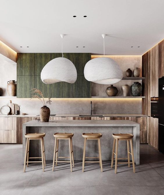 a gorgeous kitchen with stained lower and green fluted upper cabinets, a concrete kitchen island, wooden stools and statement vases