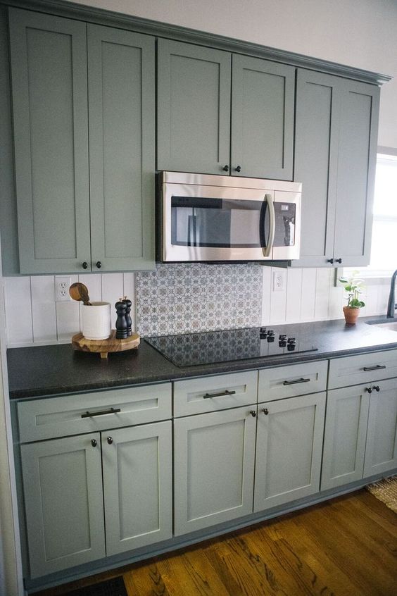 a green shaker style kitchen with a beadboard backsplash and black countertops plus built-in appliances