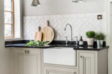 a greige farmhouse kitchen with shaker cabinets, a white tile backsplash, a black countertop and lovely metallic sconces