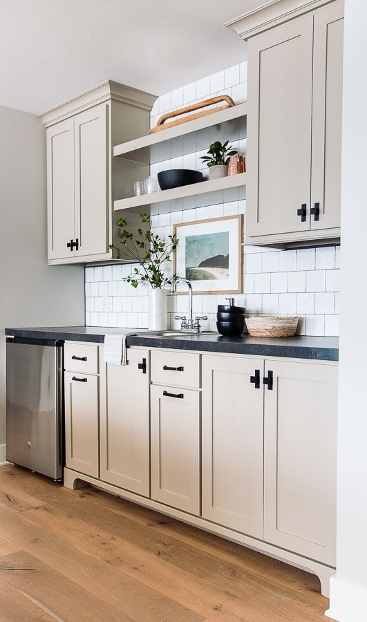 a greige kitchen with a white square tile backsplash, open shelves, and black countertops is a stylish space with a farmhouse feel