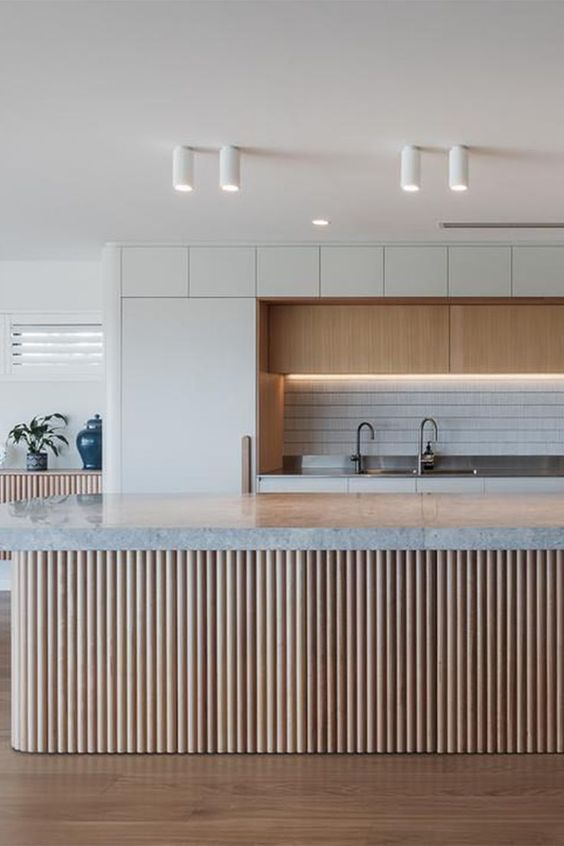 a large contemporary kitchen with lit up upper cabinets, a tile backsplash, a ridged kitchen island with a grey stone countertop