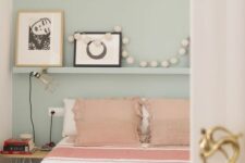 a light blue bedroom with a bed with pink and white bedding, an open shelf and a nightstand plus black and white artwork