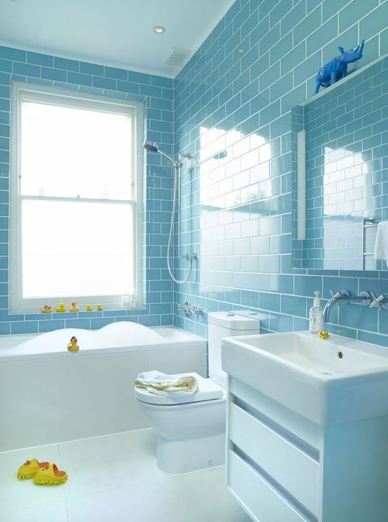 a light blue subway tile clad bathroom with white fixtures and appliances, yellow ducks for fun