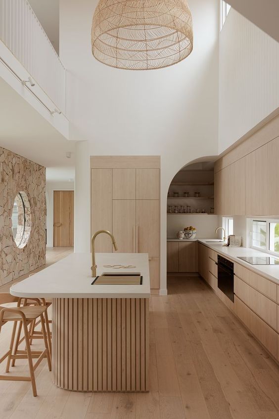 a light stained minimalist kitchen with sleek cabinets, a window backsplash, a fluted kitchen island with a curved part and a woven pendant lamp