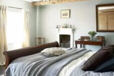 a lovely Provence bedroom with wooden beams, a fireplace, a dark stained bed and a mirror plus some vintage furniture