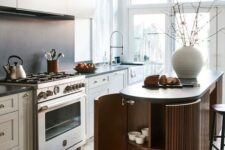 a lovely Scandinavian kitchen dove grey cabinets, a matte black backsplash, a ridged curved kitchen island and pendant lamps over it