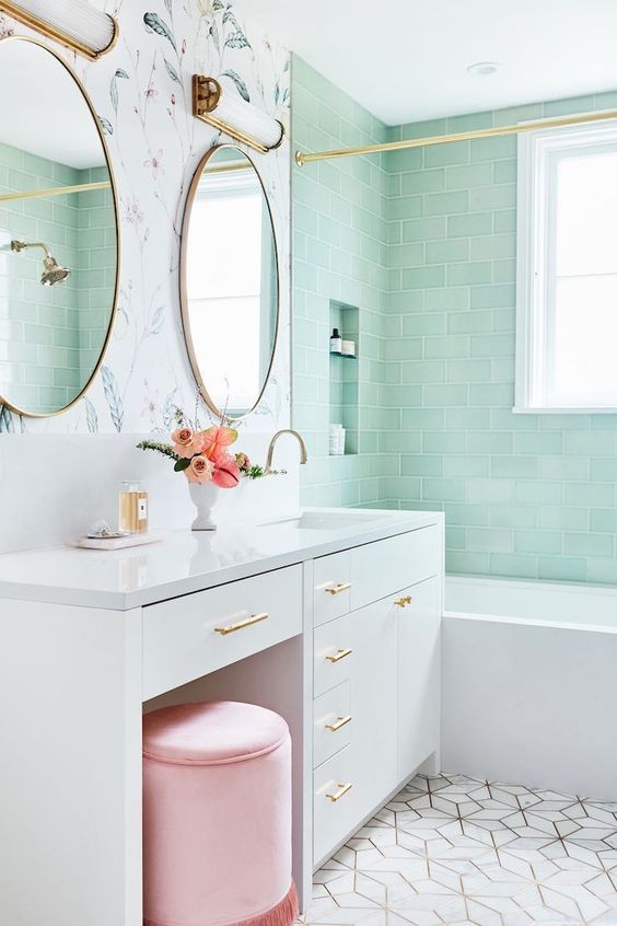 a lovely bathroom with mint green tiles, a flower wall, geo tiles on the floor, a large vanity and a pink pouf