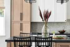 a lovely farmhouse kitchen with stained and white kitchen cabinets, black countertops, pendant black frame lamps
