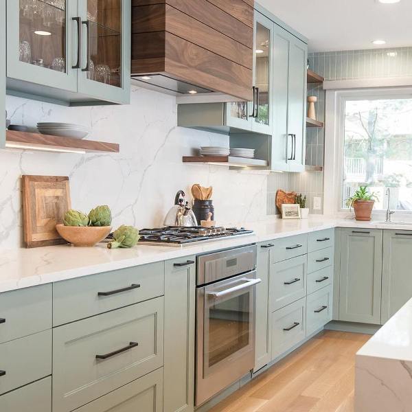 a lovely light green kitchen with shaker cabinets, open shelves, a white quartz backsplash and countertops and a matching kitchen island