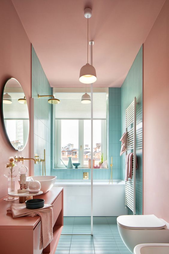 a lovely pastel bathroom with turquoise and pink walls, a pink vanity, brass and gold fixtures and a lovely view