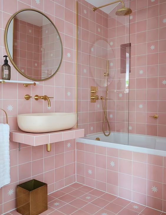 a lovely pink bathroom with pink star tiles, a floating vanity, a tub, gold fixtures and details