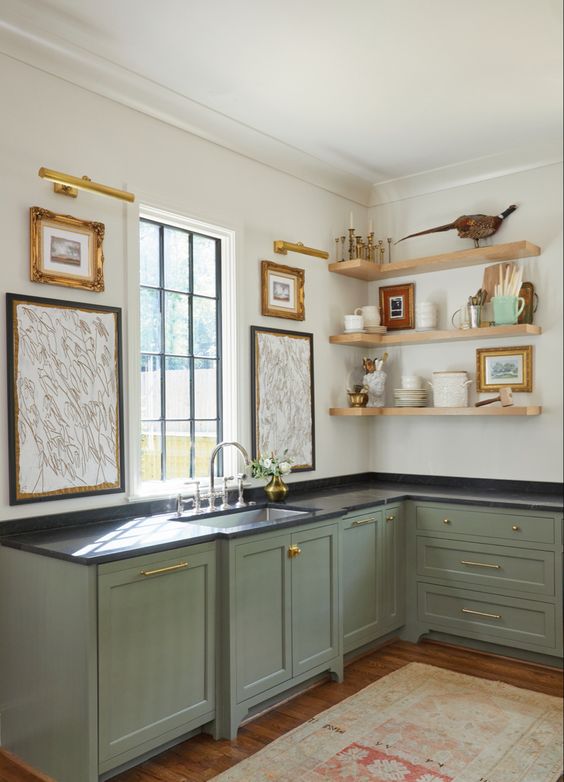a lovely sage green kitchen with shaker cabinets with black countertpos, open shelves, vintage artwork is pure elegance