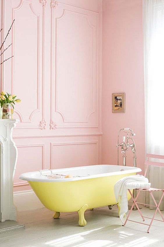 a lovely vintage pastel bathroom with pink walls, a light green fireplace, a pink chair and a yellow clawfoot tub