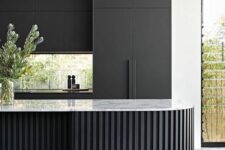 a matte black kitchen with no handles, a window backsplash, a curved and ridged black kitchen island with a white stone countertop