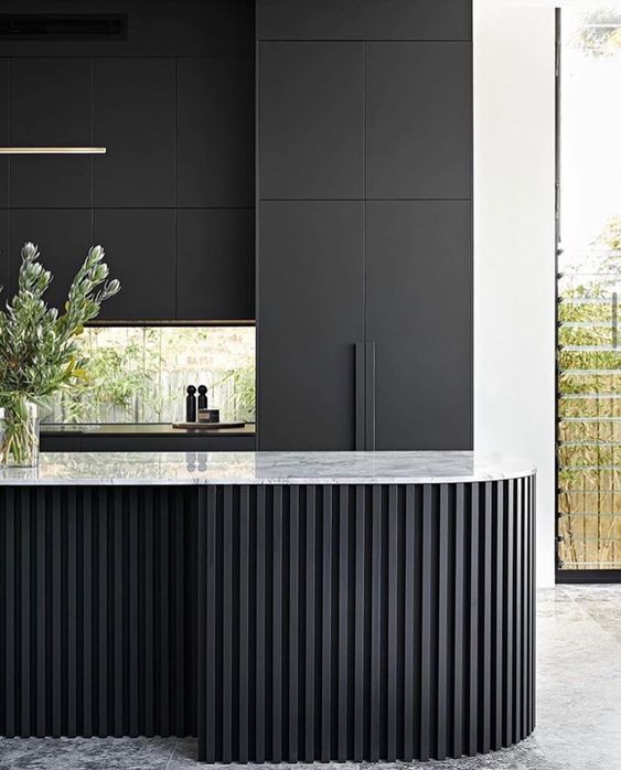 a matte black kitchen with no handles, a window backsplash, a curved and ridged black kitchen island with a white stone countertop