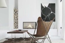 a minimal space with a built-in fireplace, firewood, a black and white artwork, a stained table and a leather butterfly chair