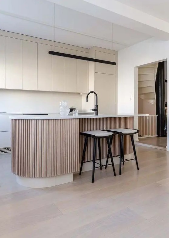 a minimal tan kitchen with matte plain cabinets, a matching backsplash and a ribbed kitchen island with a black faucet as an accent