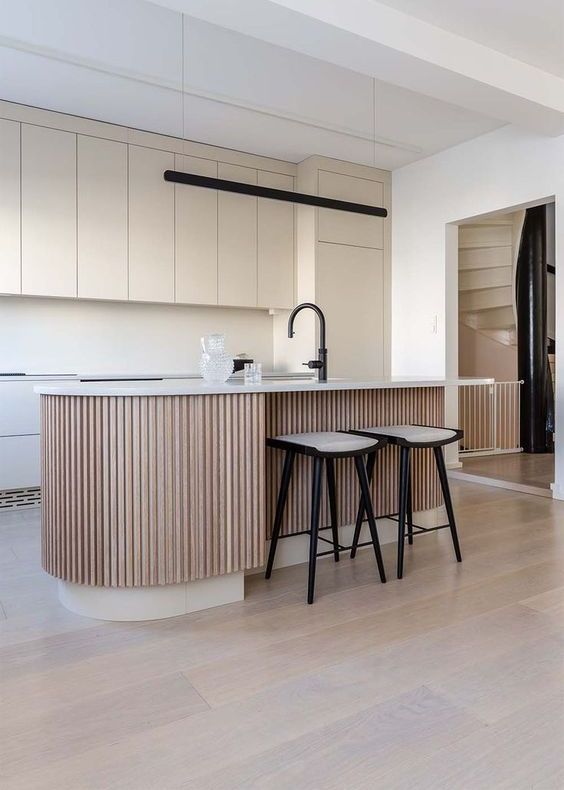 a minimal tan kitchen with matte plain cabinets, a matching backsplash and a ribbed kitchen island with a black faucet as an accent