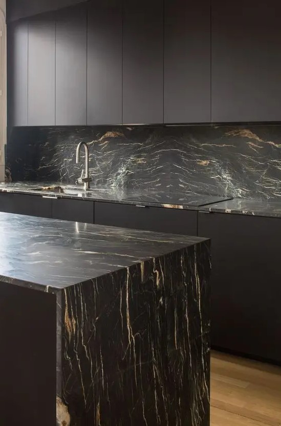 a minimalist black kitchen with sleek cabinets, black marble countertops and a backsplash and neutral fixtures