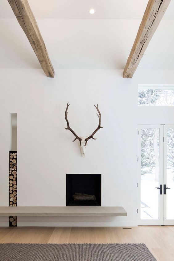 a minimalist fireplace wiht a concrete detail, a firewood storage niche and antlers is a great idea for a minimalist space