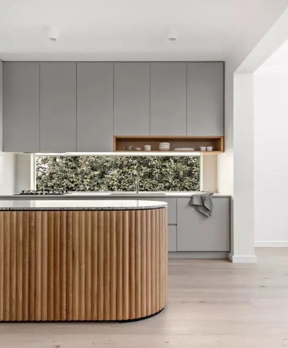 a minimalist grey kitchen with a window backsplash and a curved fluted kitchen island with a terrazzo countertop looks ultimate