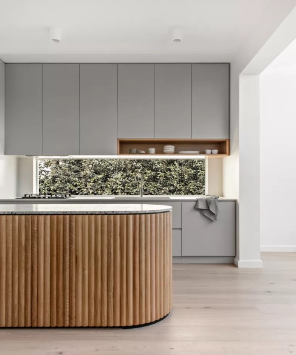 a minimalist grey kitchen with a window backsplash and a curved fluted kitchen island with a terrazzo countertop looks ultimate